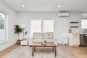 A modern living room with a sofa, coffee table, and a kitchen area with a fridge and cabinets.