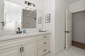 A modern bathroom with a white vanity, a large mirror, and a shower area.