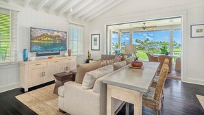 A spacious living room with a large TV, comfortable seating, and a view of the outdoors. - Golf Course View | Resort Amenities | Outdoor Shower (Koloa)