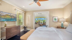 A hotel room with a large bed, a ceiling fan, a dresser, and a view of the outdoor seating area. - Golf Course View | Resort Amenities | Outdoor Shower (Koloa)