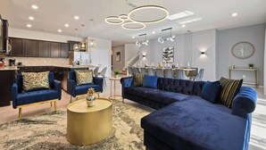 Ein modernes Wohnzimmer mit einem blauen Sofa, zwei Sesseln, einem Couchtisch und einem Essbereich im Hintergrund.
