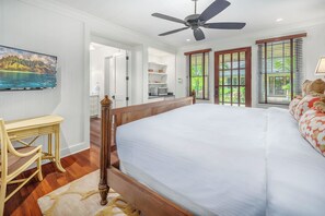 Une chambre avec un grand lit, un ventilateur de plafond et un téléviseur fixé au mur.