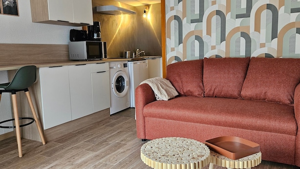 Un espace de vie compact comprenant un canapé, une table basse ronde en bois, un lave-linge, un four à micro-ondes et une chaise.