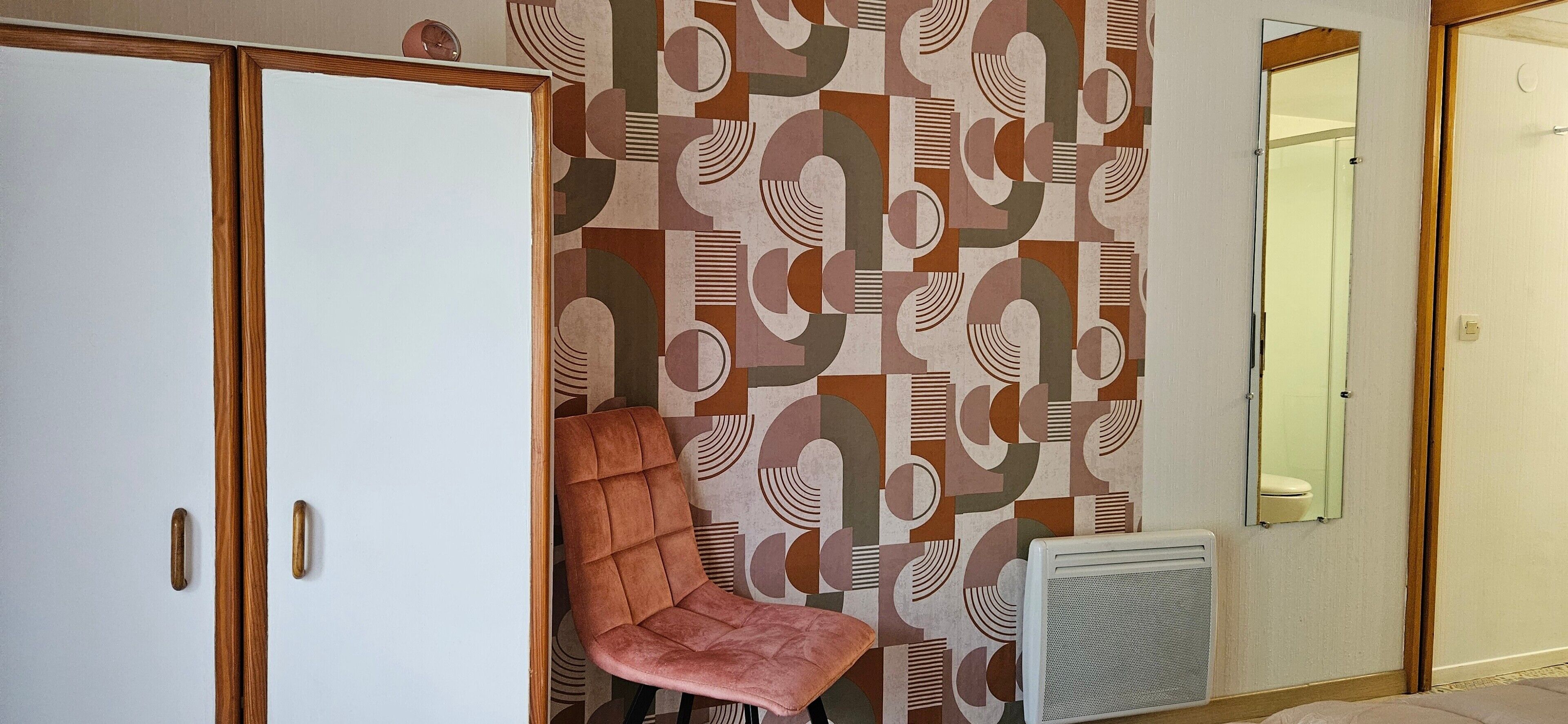 Een kamer met een patroonmuur, een stoel, een radiator en een kledingkast.