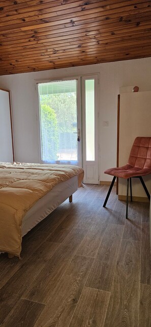 Une pièce avec un lit, une chaise, un plafond en bois et une fenêtre.