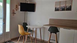 Une petite cuisine équipée avec un téléviseur, deux chaises, une table et une fenêtre donnant sur un paysage verdoyant.