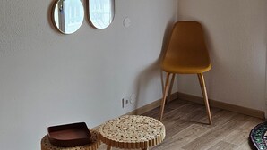 Une pièce avec un plafond en bois, une horloge murale et trois miroirs. On y trouve deux tables rondes avec des tabourets, dont l’un est doté d’un siège en osier tressé.