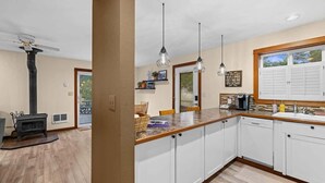 Eine Küche mit weißen Schränken, einer Holzausziehtafel, Pendelleuchten, einem Herd und einem Fenster mit Jalousien.