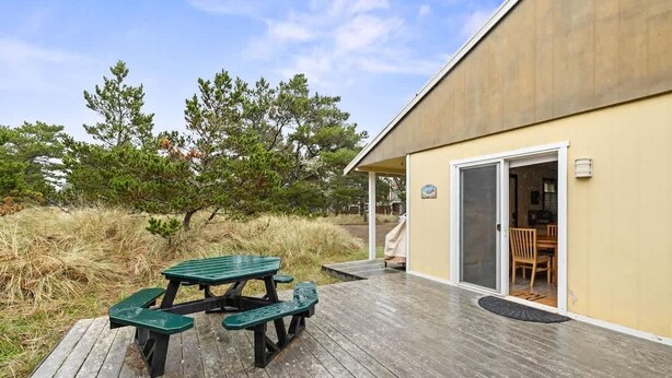 Eine Holzterrasse mit Picknicktischen, einer überdachten Terrasse und einem Gebäude mit einer Glastür.