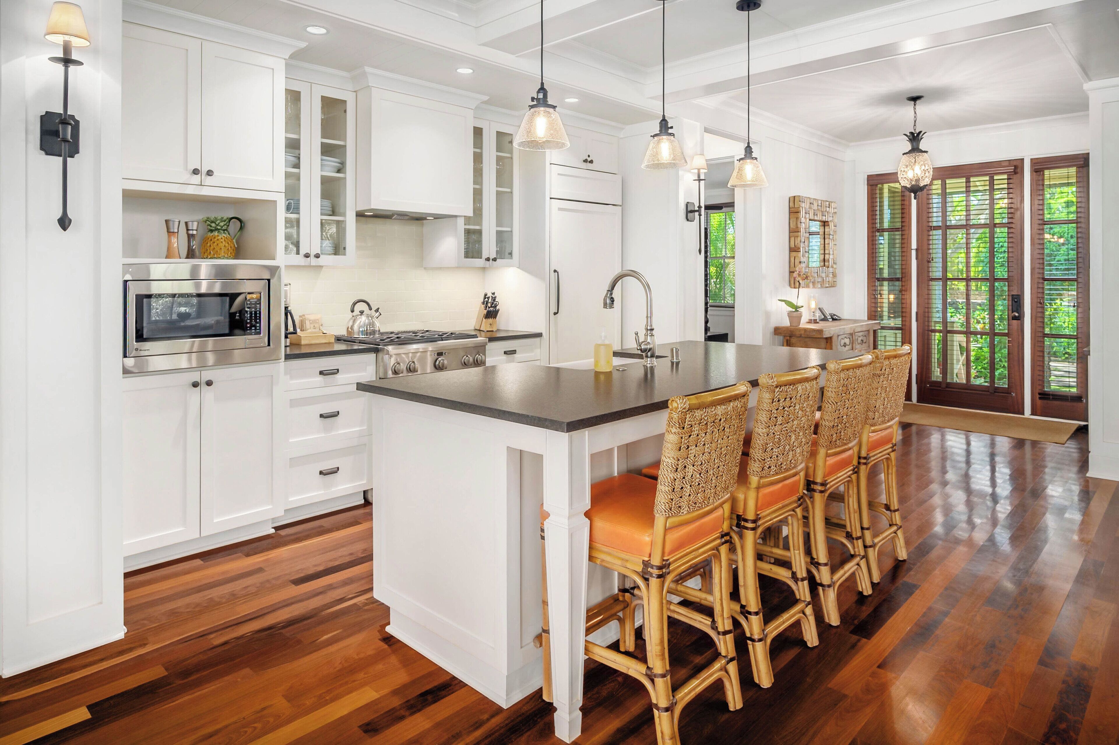 A modern kitchen with white cabinetry, a central island with bar stools, stainless steel appliances, and pendant lighting.