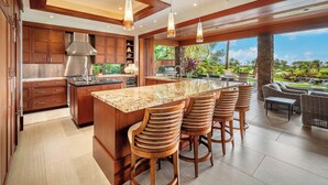 A spacious kitchen with a large island, wooden bar stools, and a view of a lush garden.