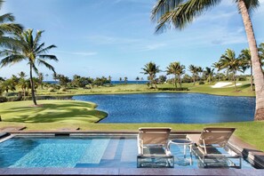 A poolside view with a golf course and ocean in the background.