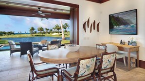 Un coin repas avec une table ronde et des chaises, une vue sur un terrain de golf et sur l’eau, et un tableau accroché au mur.