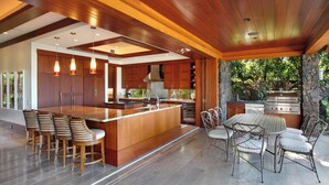 Una cucina moderna con un'isola grande, sgabelli da bar e una zona barbecue esterna.