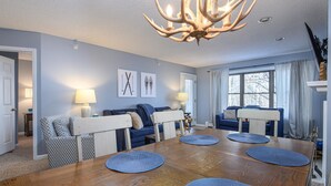 A dining area with a wooden table, blue placemats, and a chandelier. - Ski-In/Out Winterplace Okemo Mountain Condo-Bldg M (Ludlow)