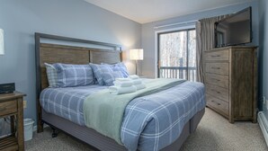 A bedroom with a bed, bedside table, lamp, dresser, and a TV on a stand. - Ski-In/Out Winterplace Okemo Mountain Condo-Bldg M (Ludlow)
