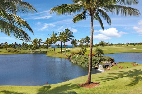 A golf course with a pond, palm trees, and a small waterfall.