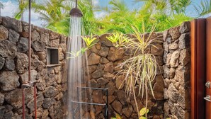 Eine Dusche mit Steinwänden, einem Wasserhahn, einem kleinen Fenster und tropischen Pflanzen.