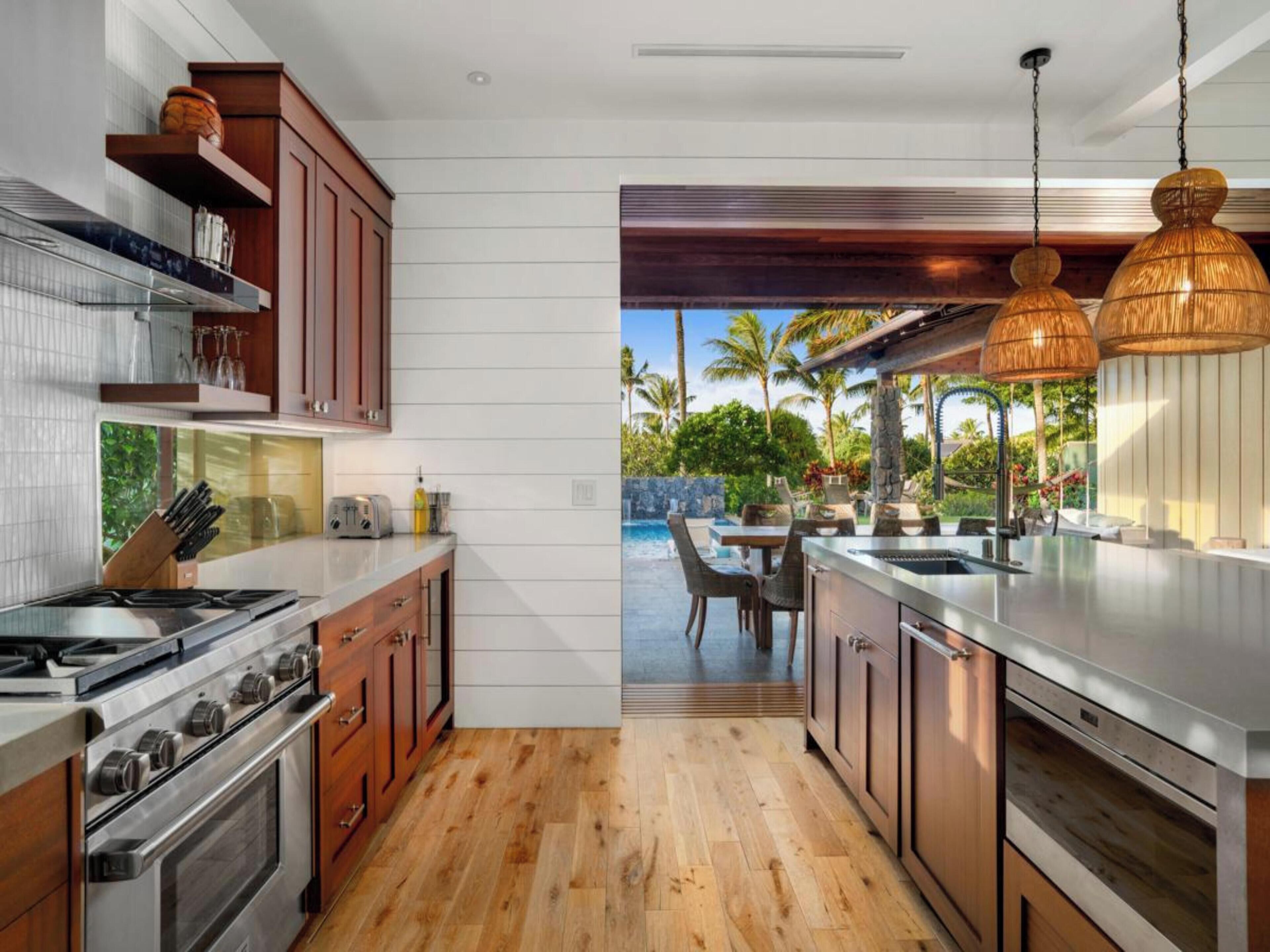 A modern kitchen with wooden cabinets, a stainless steel stove, and a view of a pool area with outdoor furniture.