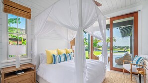 Camera da letto con un letto a baldacchino, un comodino in legno, una sedia in vimini e vista su piscina e vegetazione.