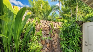 A garden with a stone wall, tropical plants, and a water feature. - Resort Amenities | Firepit & Outdoor Shower (Koloa)