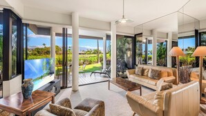 A spacious living room with a large window offering a view of a lush garden and distant mountains. - Mauna Lani Point B102 is a Golfer's Dream w/Fairway and Ocean Views | CoralTree (Kohala Coast)