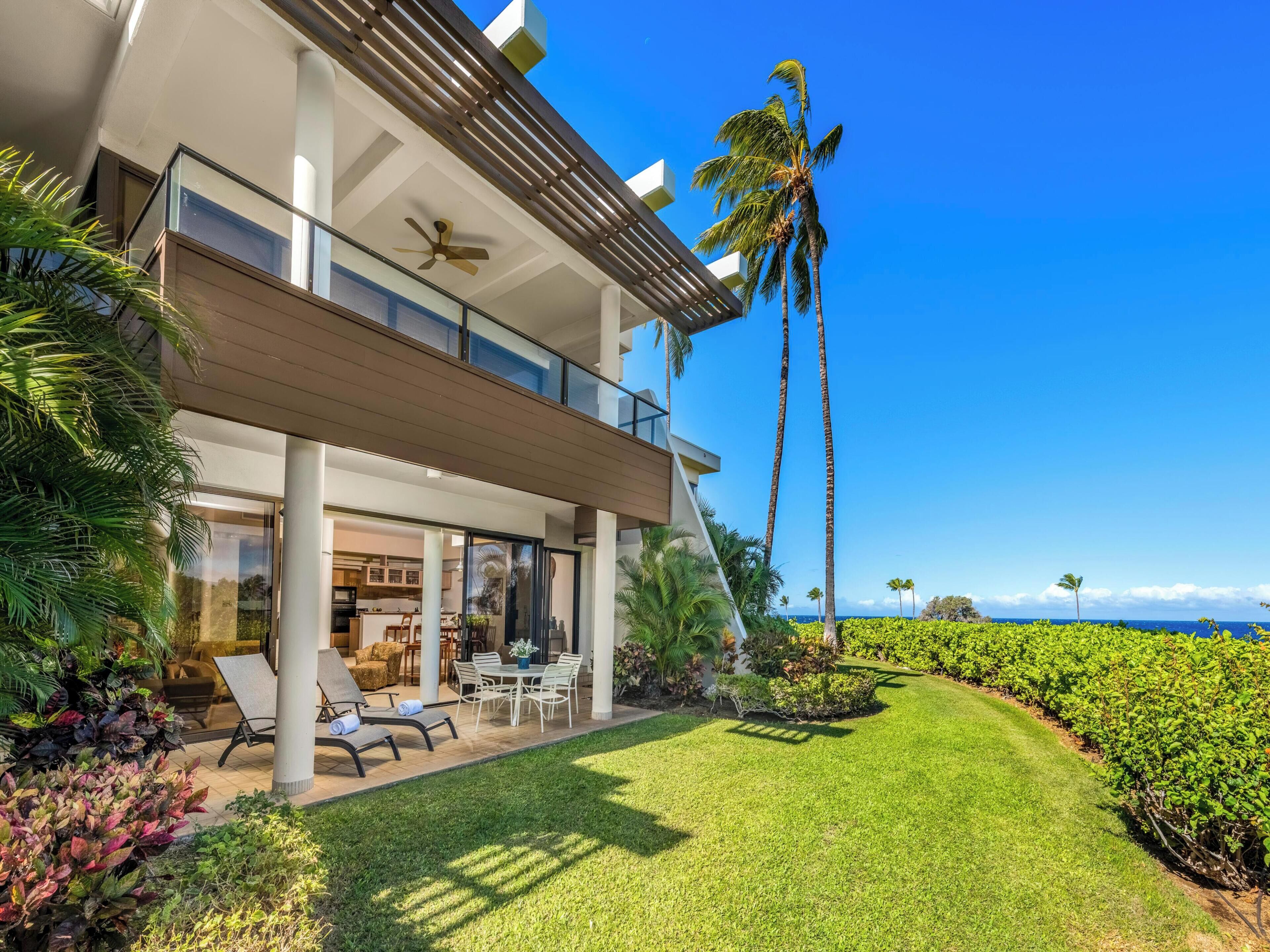 A modern two-story house with a balcony, a patio with outdoor furniture, and a well-maintained lawn.
