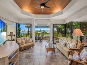 A spacious living area with a large window offering a view of a golf course and mountains. - *CoralTree Managed* Ocean View on Top-Rated Golf Course | Mauna Lani Point B201 (Kamuela)