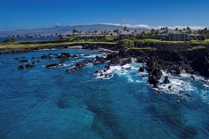 A coastal hotel with ocean views, rocky shoreline, and a golf course in the background.