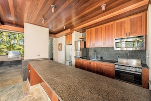 A modern kitchen with granite countertops, wooden cabinets, stainless steel appliances, and a stone backsplash.