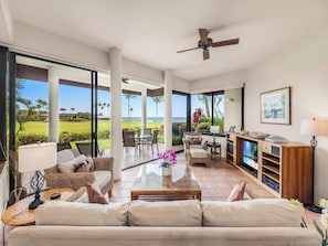 A spacious living area with a view of a golf course and ocean, featuring a sofa, coffee table, and a television.