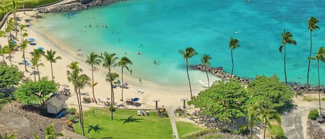 A coastal resort with a sandy beach, palm trees, and a clear blue sea.