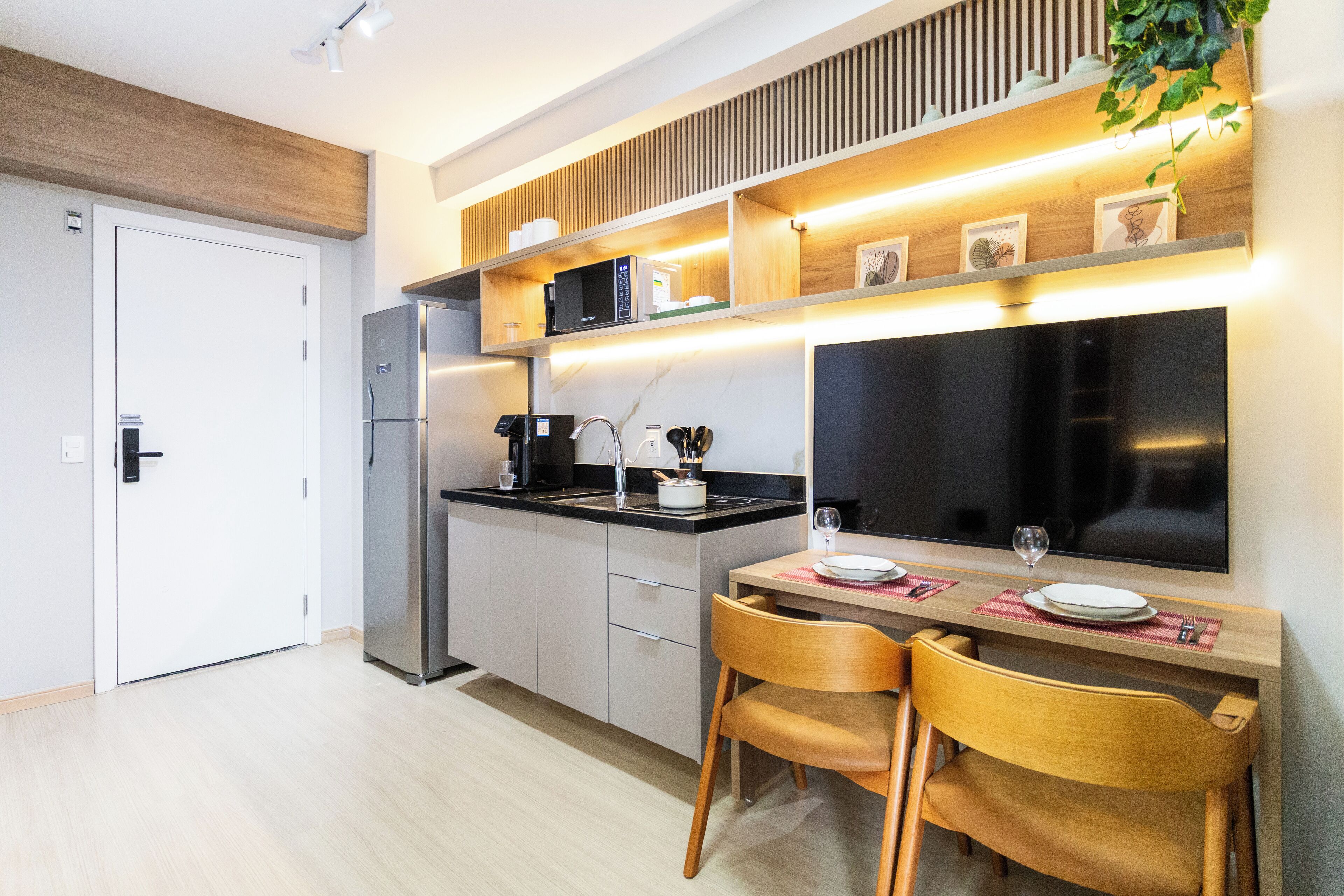 Une cuisine moderne équipée d’un four à micro-ondes encastré, d’un réfrigérateur et d’un coin repas avec deux chaises et une table dressée pour deux personnes.