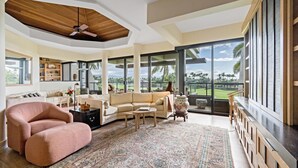 Ein geräumiges Wohnzimmer mit großem Fenster und Blick auf einen Golfplatz, Deckenventilator und moderner Kamin.