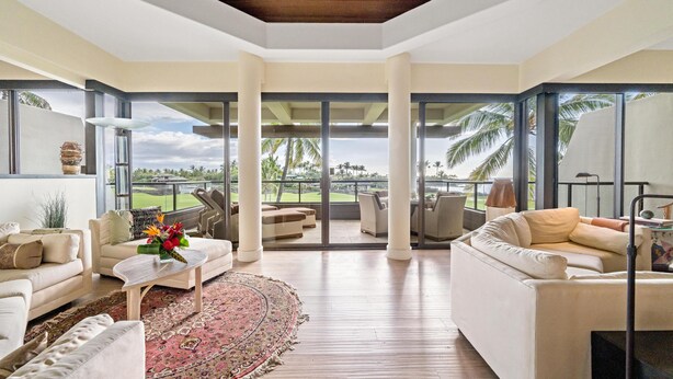 Ein geräumiger Wohnbereich mit großem Fenster und Blick auf einen Golfplatz. Mehrere Sofas und ein Couchtisch mit einer dekorativen Vase sind vorhanden.