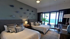 A hotel room with two beds, a nightstand with a lamp, a desk with a chair, and a view of the ocean through large windows. - Iyari Luxury Villa: 4BR, Private Pool & Premier Access (Punta Mita)