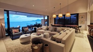 A modern living room with a large sofa, a dining area, and a view of the sea. - Iyari Luxury Villa: 4BR, Private Pool & Premier Access (Punta Mita)