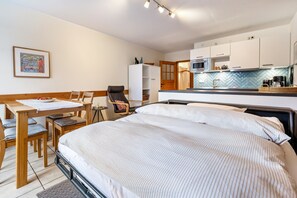 Une chambre d’hôtel comprenant un lit, un bureau avec des chaises, une kitchenette et une porte donnant sur une salle de bain.