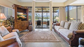 A spacious living area with a large flat-screen TV, comfortable seating, and a view of the outdoors. - Mauna Lani Point H207 - Includes Membership to Nearby Luxury Fitness Club! (Kamuela)