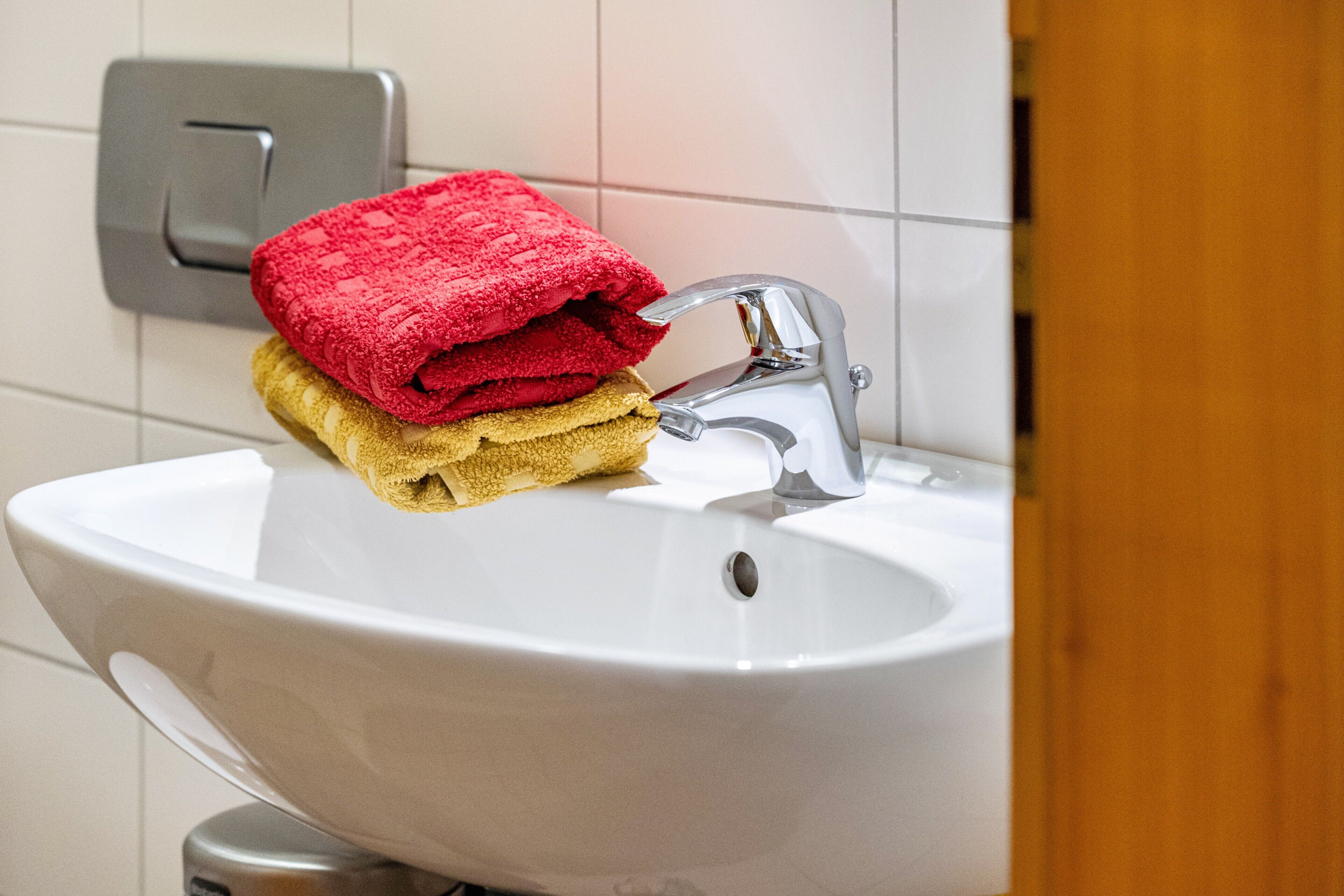 Un évier blanc avec un robinet chromé, une serviette rouge et une serviette jaune pliées et posées dessus.