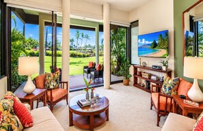 A spacious living room with a large television, comfortable seating, and a view of a golf course.