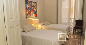A hotel room with two beds, a painting on the wall, a lamp, and a chair. - Historic 19th-century apartment with a balcony overlooking the square (Málaga)