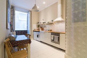 A compact kitchen with a washing machine, oven, and dining area with chairs and a table. - Historic 19th-century apartment with a balcony overlooking the square (Málaga)
