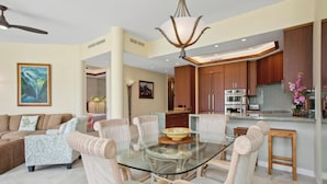 A modern living room with a glass dining table surrounded by wicker chairs, a sofa, and a ceiling fan. - Mauna Lani Point J104 | Pool | Hot Tub | Resort Amenities | CoralTree Managed (Kamuela)