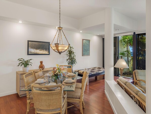 A dining area with a glass-top table, wicker chairs, and a hanging light fixture.