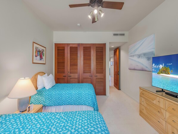 A bedroom with two beds, a ceiling fan, a TV, and a wooden wardrobe.