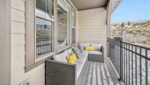 A covered porch with a gray wicker sofa, yellow pillows, and a view of a hilly landscape. - Wasatch Lodge (Heber City)