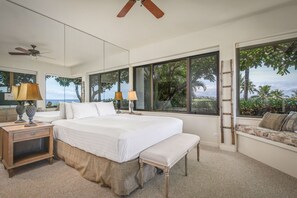Une chambre à coucher avec un grand lit, deux tables de chevet avec des lampes, un banc, une échelle et une vue sur l’extérieur grâce à de grandes fenêtres.