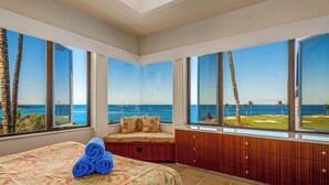 A bedroom with a large bed, a seating area with a view of the ocean, and a wooden cabinet.