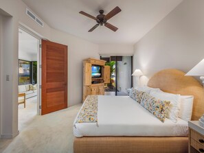 A bedroom with a bed, a wooden cabinet with a TV, a ceiling fan, and a view of a balcony.